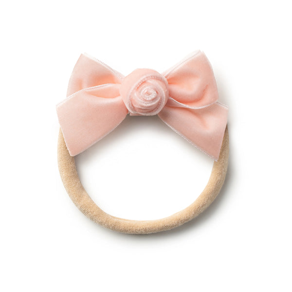 A ballet slipper-colored velvet baby headband with a floral rosette detail and a bow at the top center.