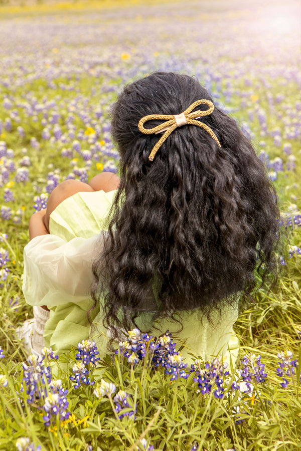Person with a bow in their hair sitting in a field of flowers