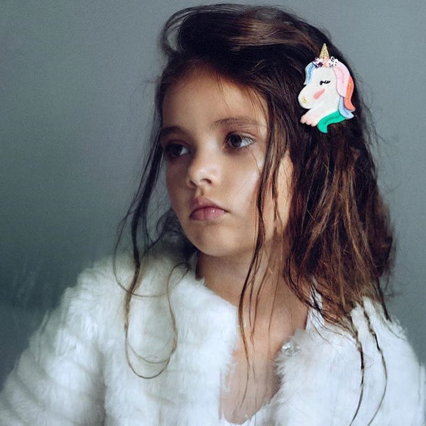 Young girl with a unicorn hair clip on a plain background