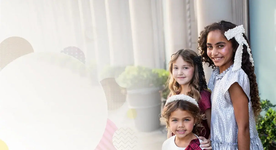 Three young girls wearing hair accessories, smiling outdoors in natural light