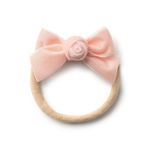 A ballet slipper-colored velvet baby headband with a floral rosette detail and a bow at the top center.