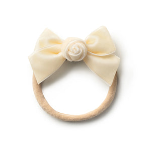 A cream colored velvet baby headband with a bow and a rosette detail.