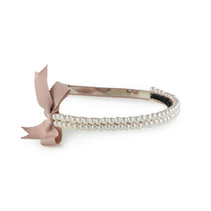 A double-strand pearl headband with a pink grosgrain bow and rubberized teeth on the inner face, set against a white background.
