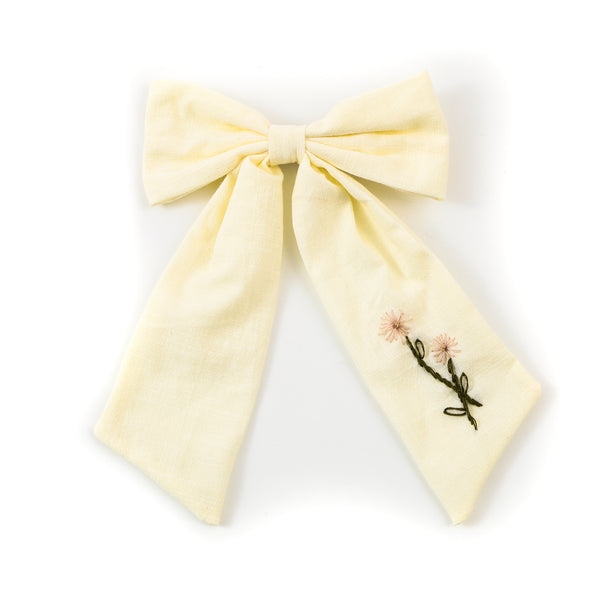 Yellow bow hair clip with floral embroidery on a white background