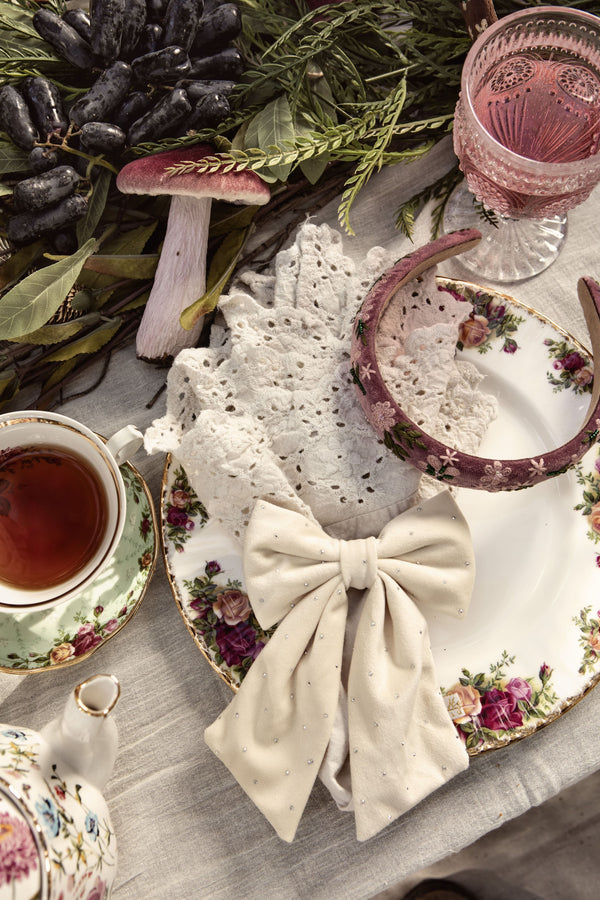 Tea party setting with lace tablecloth, teacup, and decorative elements on a wooden surface. With a floral headband.